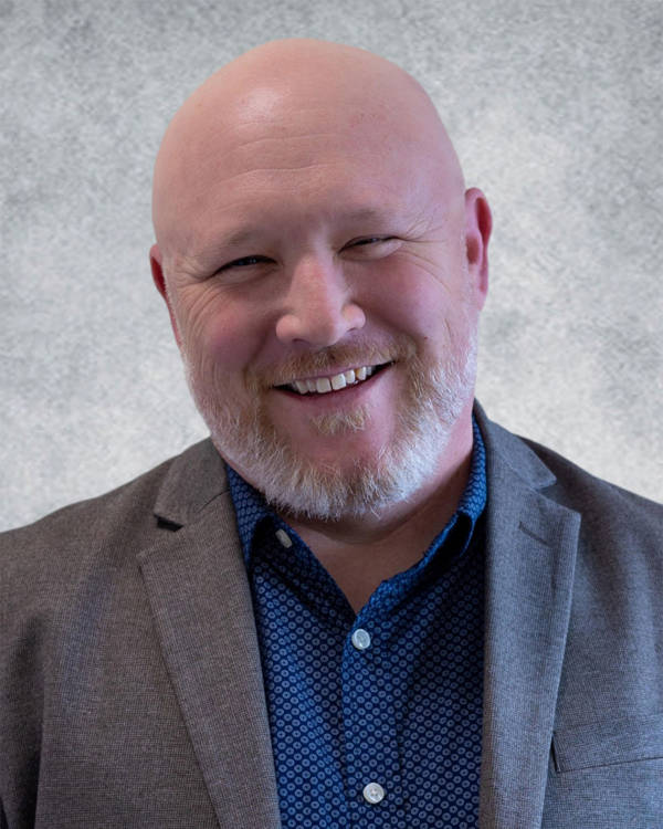 Headshot of a smiling middle aged man with light complexion, a bald head and a white and red beard.