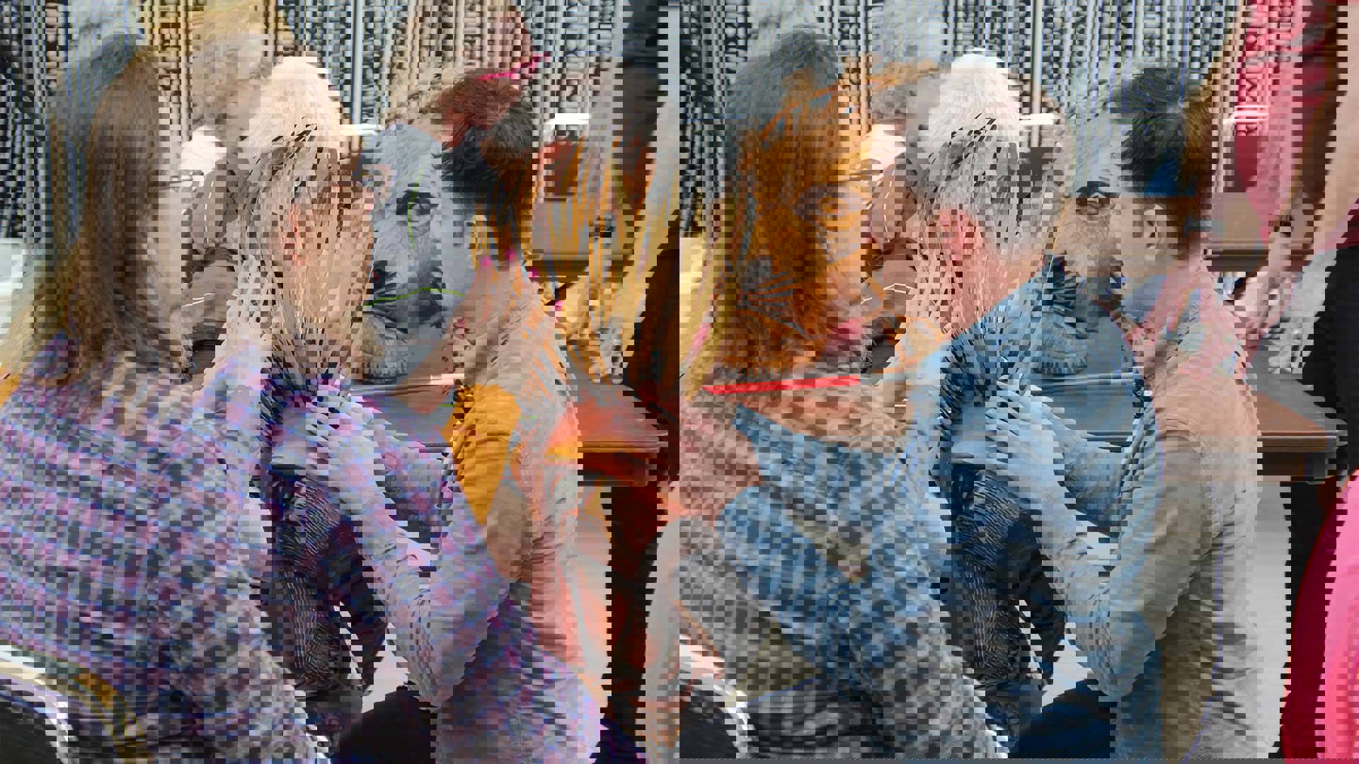 A man in a blue shirt holds a wooden lion mask and speaks to several others who are touching it
