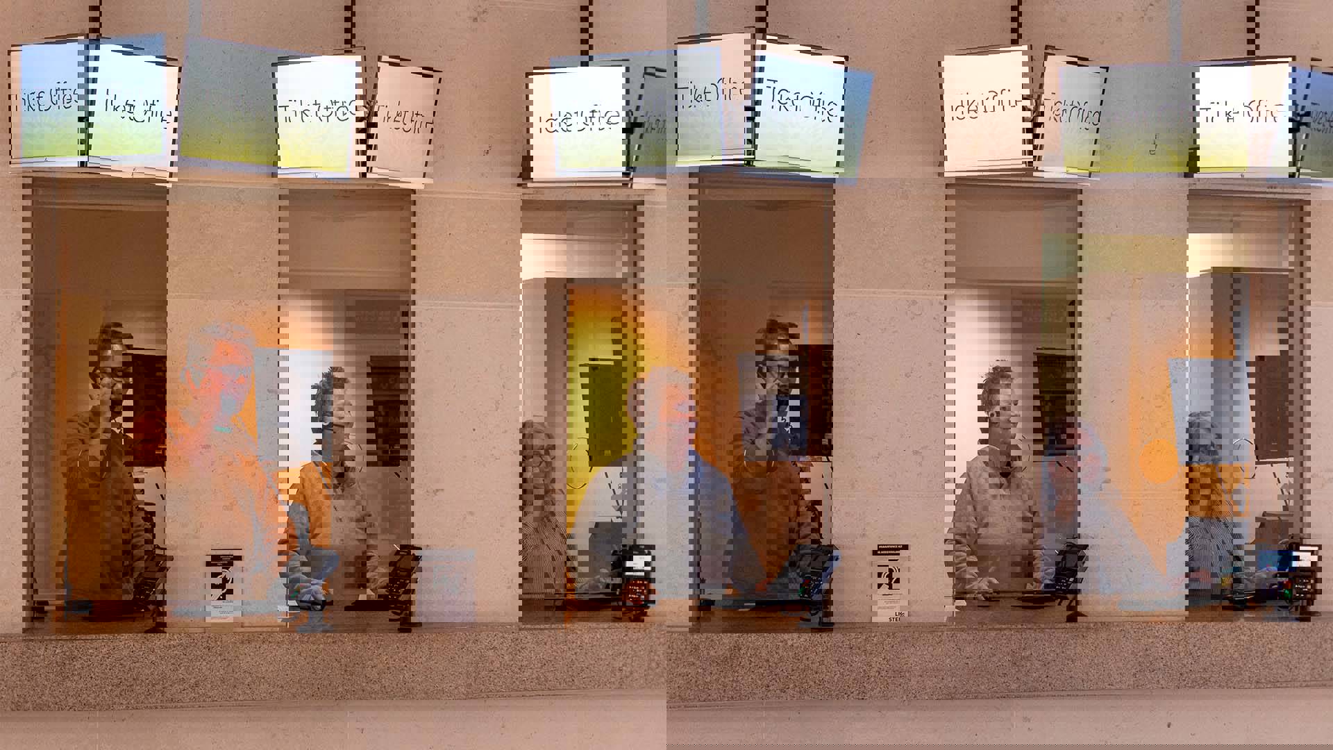 Three caucasian people working in a window each at Overture's Ticket Office. They are working on computers and talking on the phone.