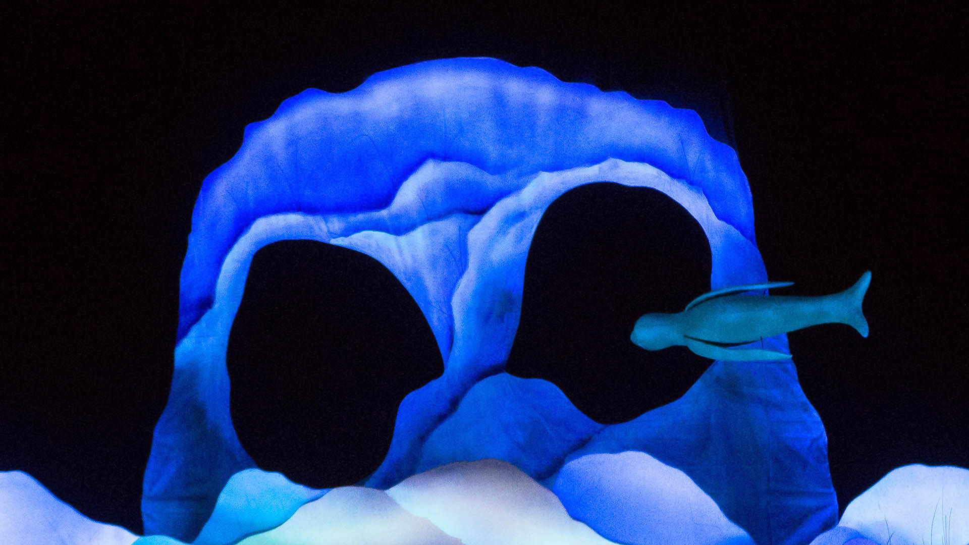 A large, blue, skull-shaped rock with a puppet of a blue, seal-shaped creature swimming through the right eye hole.