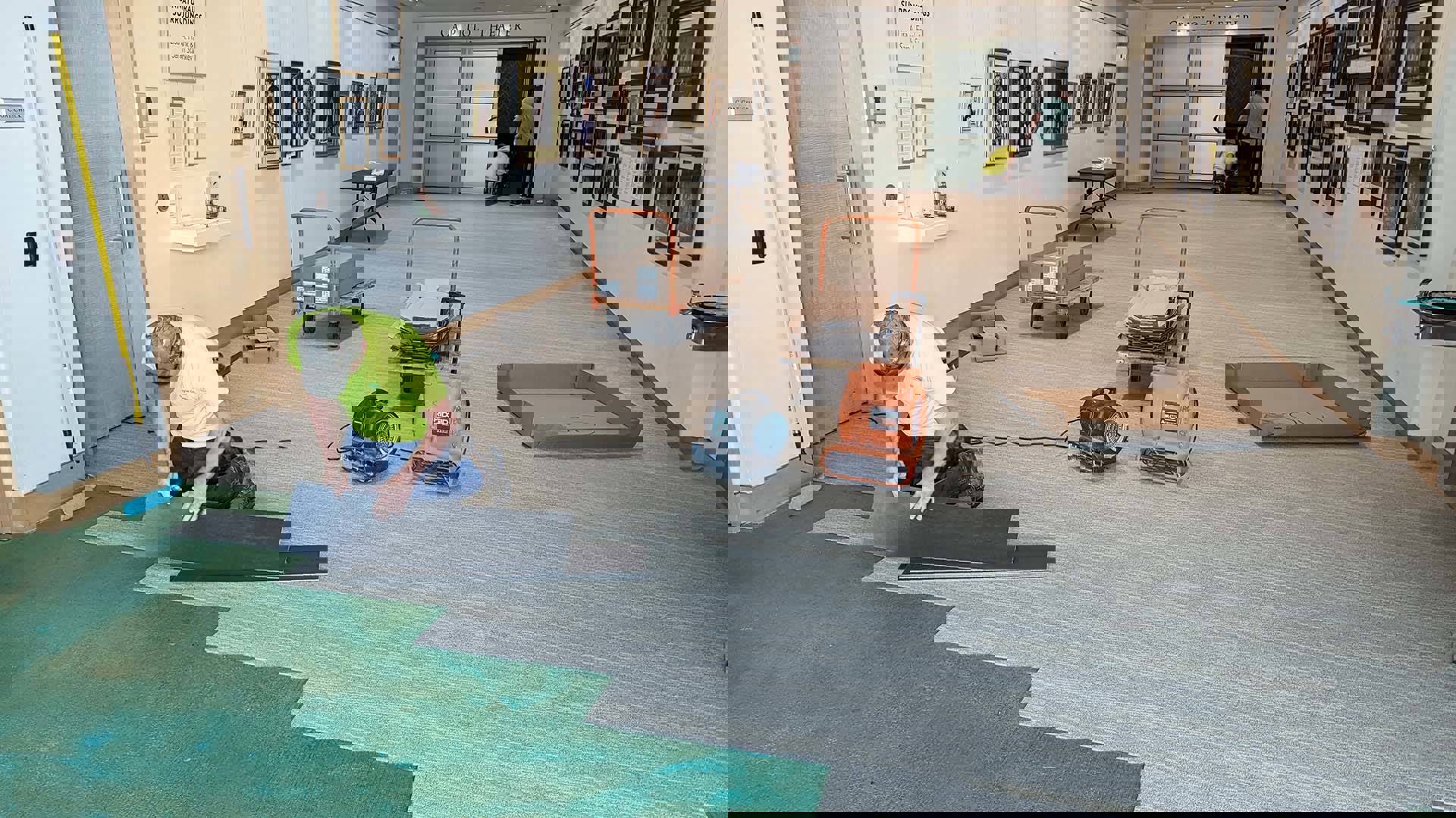 three men laying strips of tan carpet on a green floor.