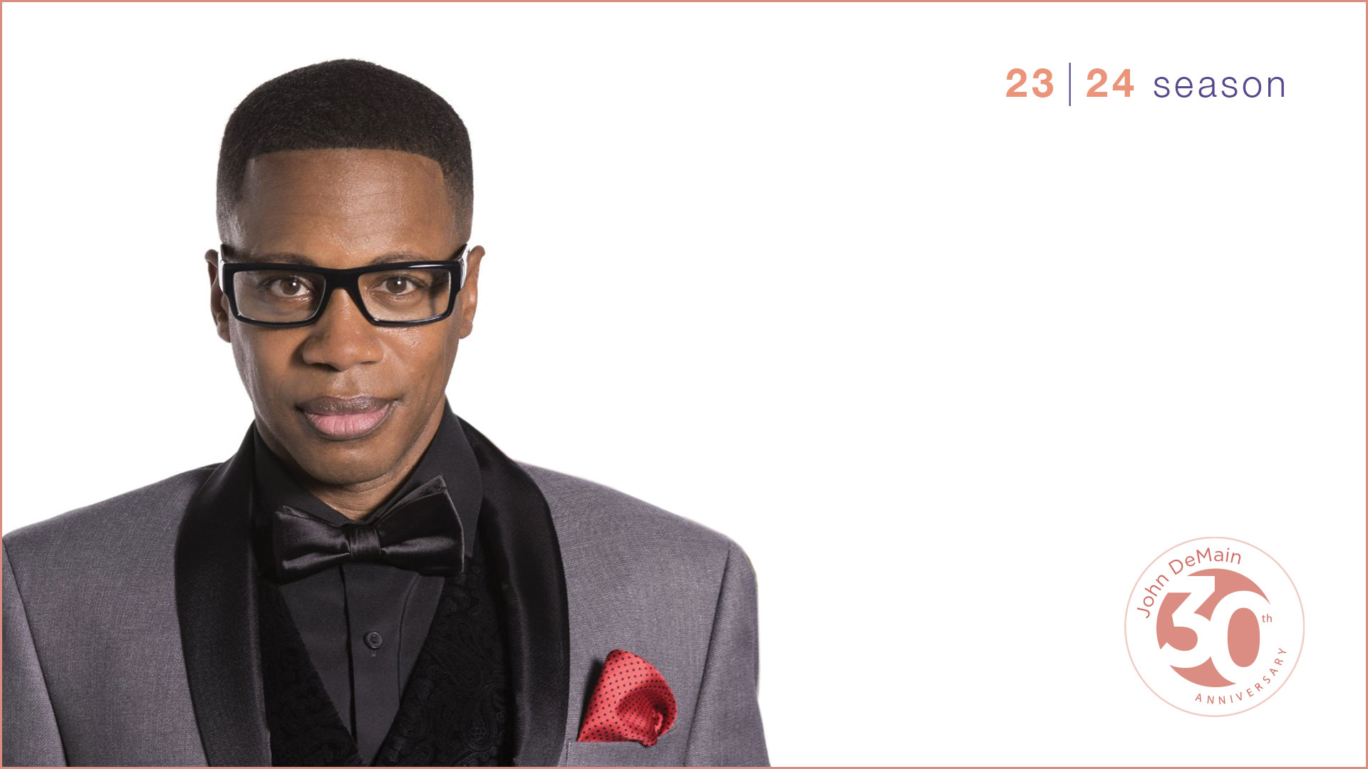 A young african american man with short hair, glasses and a silver suit with black bowtie against a white background.