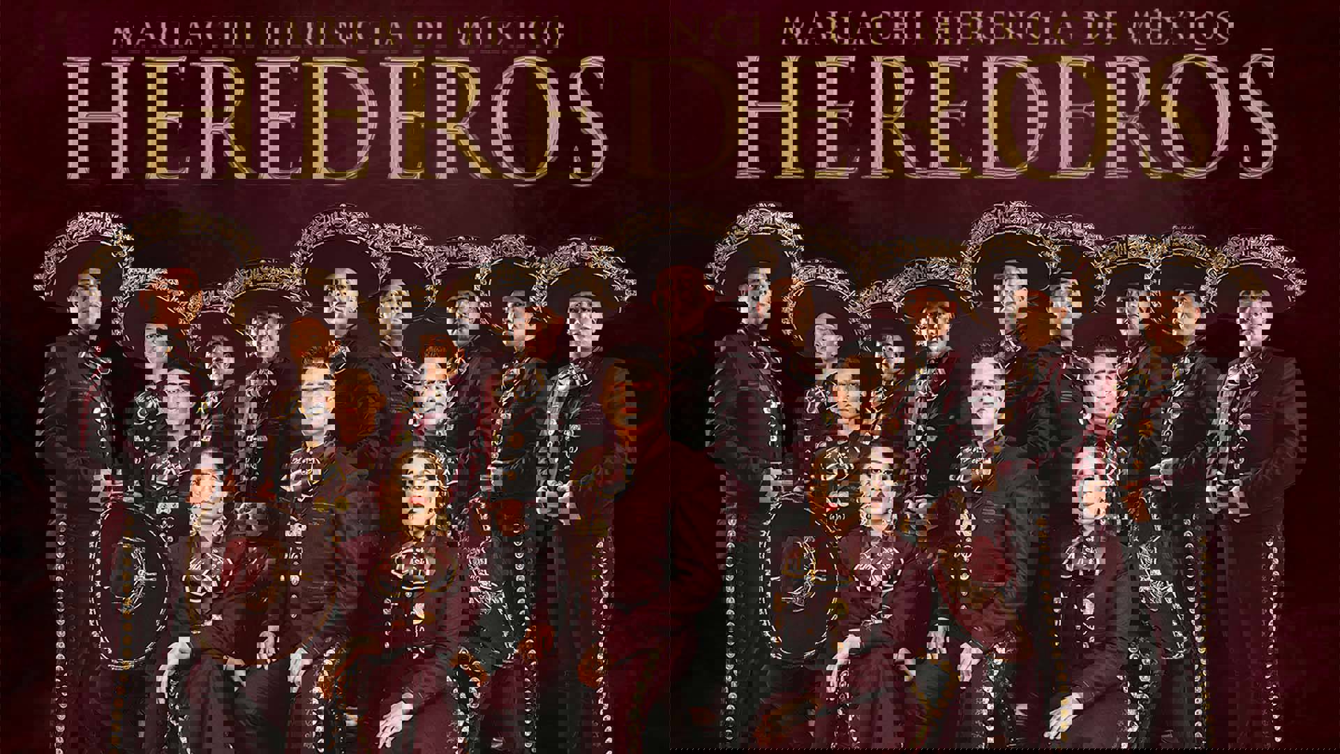 A Mariachi group in maroon Mariachi outfits. There are 14 total, with nine standing in the back with sombreros on, and five sitting in front of them. Above the group are the words "Mariachi Herencia de Mexico: Herederos". The background is a dark maroon.