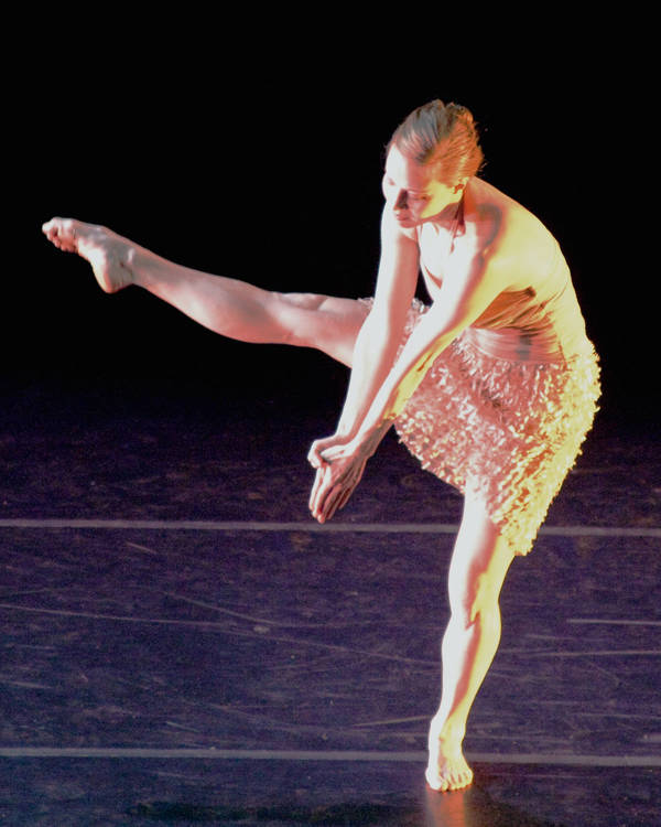 A dancer performing on a stage with gold, white and red light cast on her.