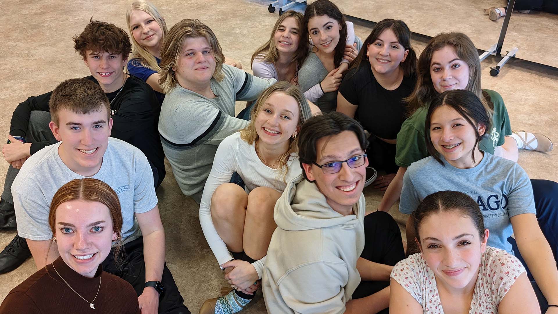 A group of smiling high school students sitting together on the ground.