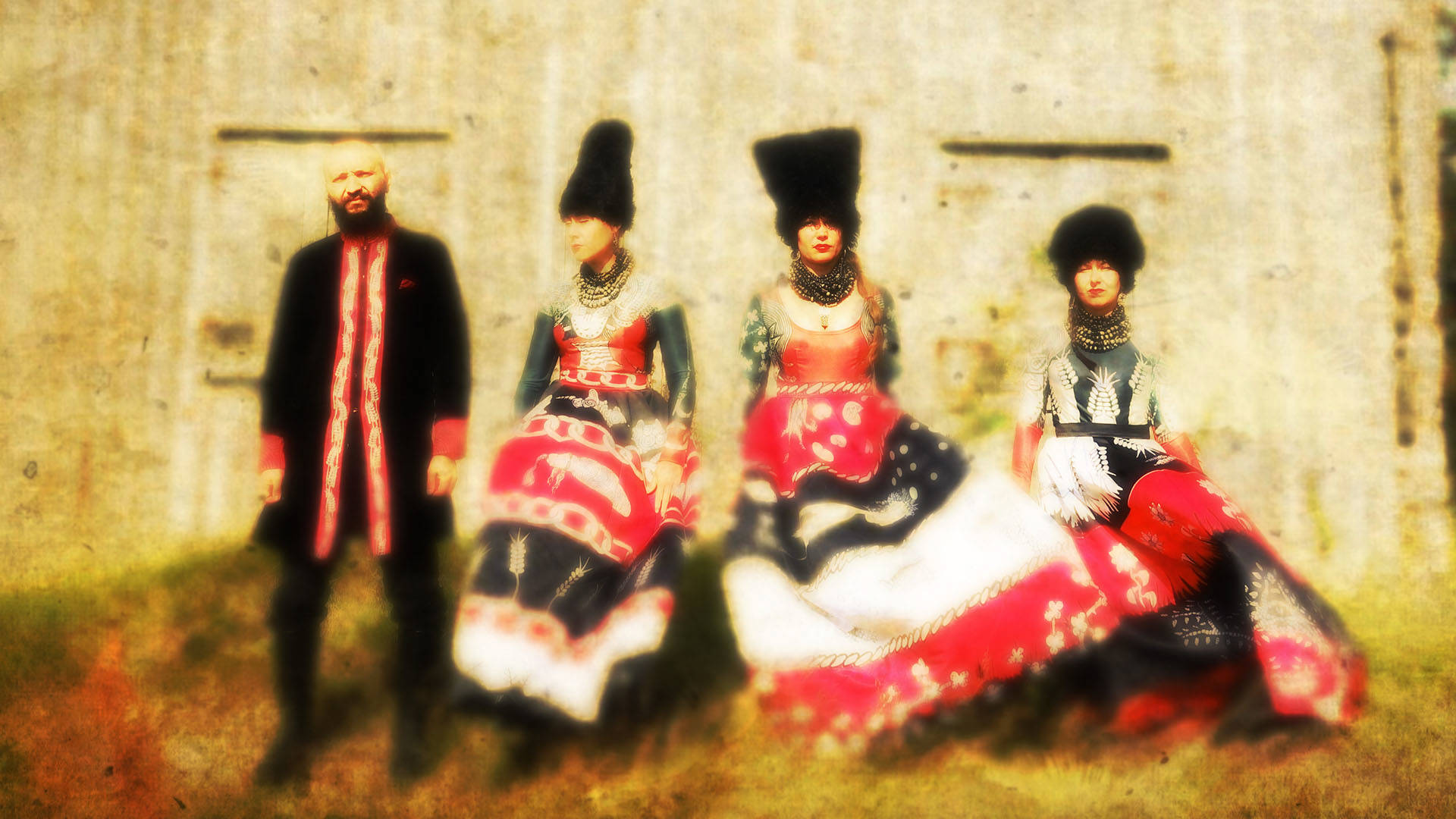 Blurry photo of four people with light complexion wearing ornate traditional black white and red Ukrainian outfits. Three have large plush black headwear on