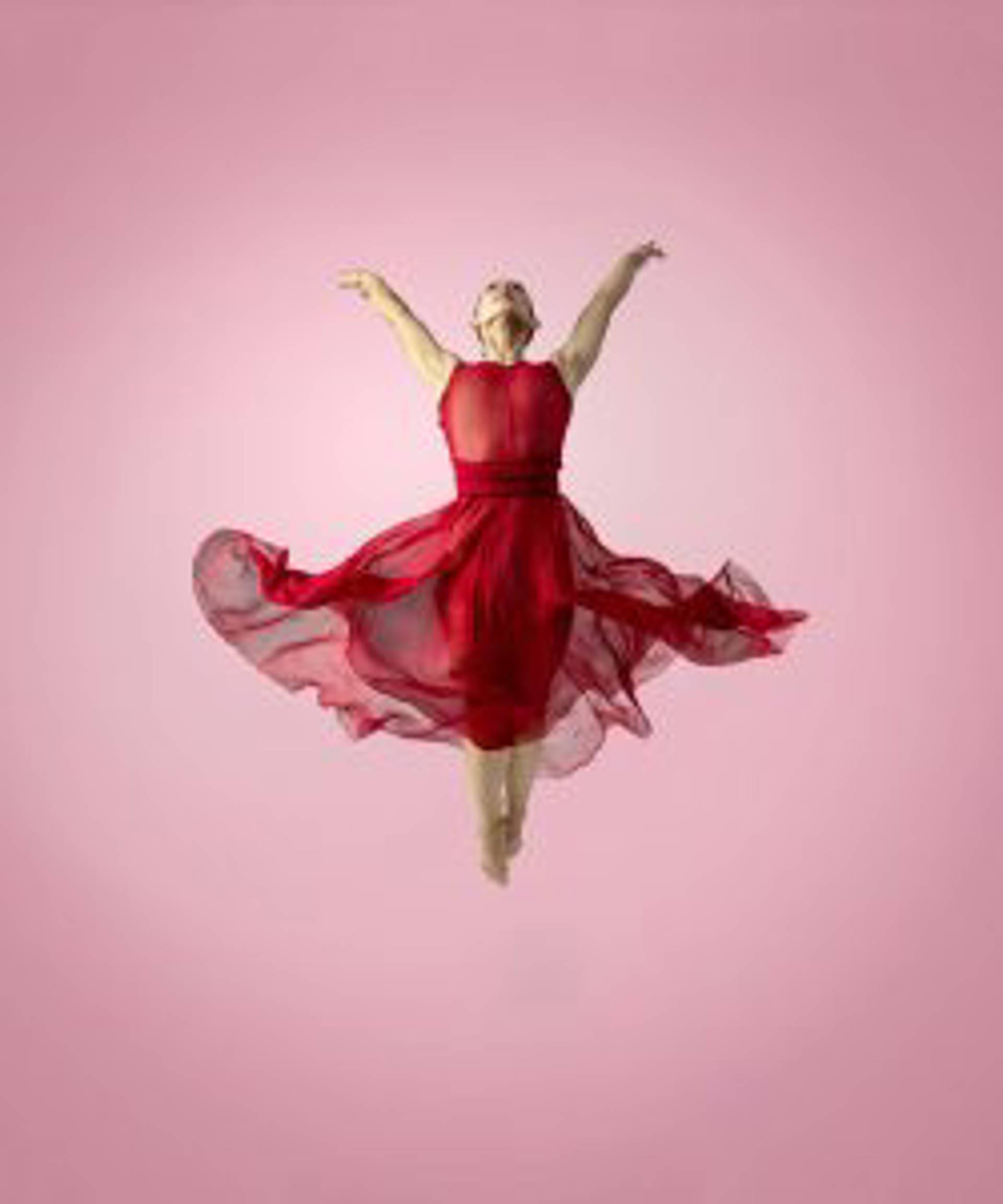 A danceer in a flowing red dress suspended against a red background.