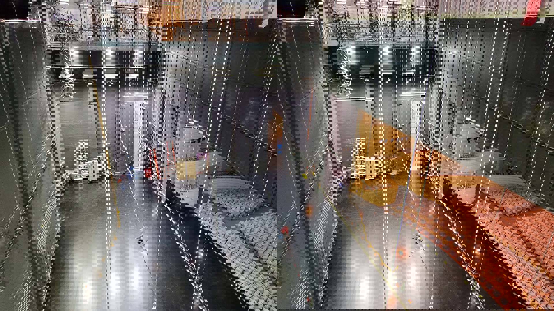 A high view of a Overture Hall stage from the scaffolding above. The stage is black and some audience seating is visible. A small worker in a red shirt is working on one of the flies.