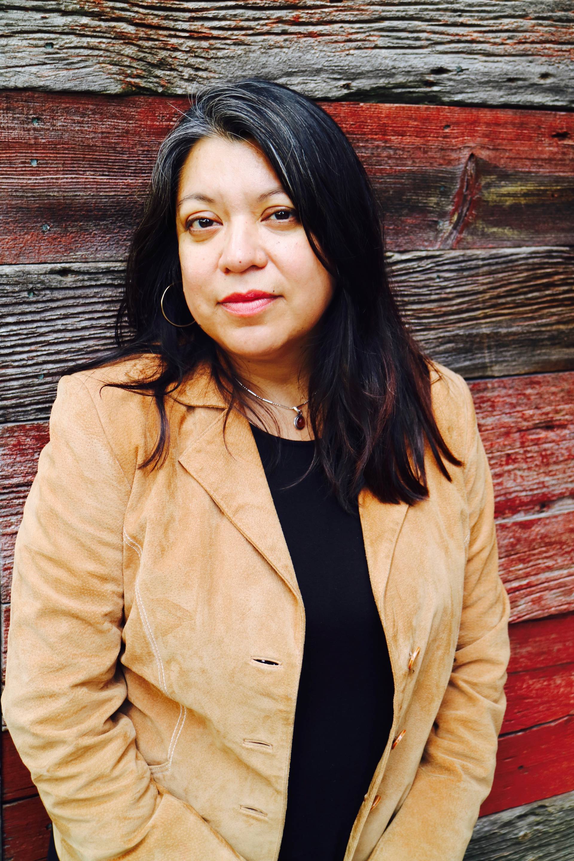 Headshot of a middle aged woman with medium complexion, brown eyes and long dark hair. She is wearing a tan jacket over a black top.