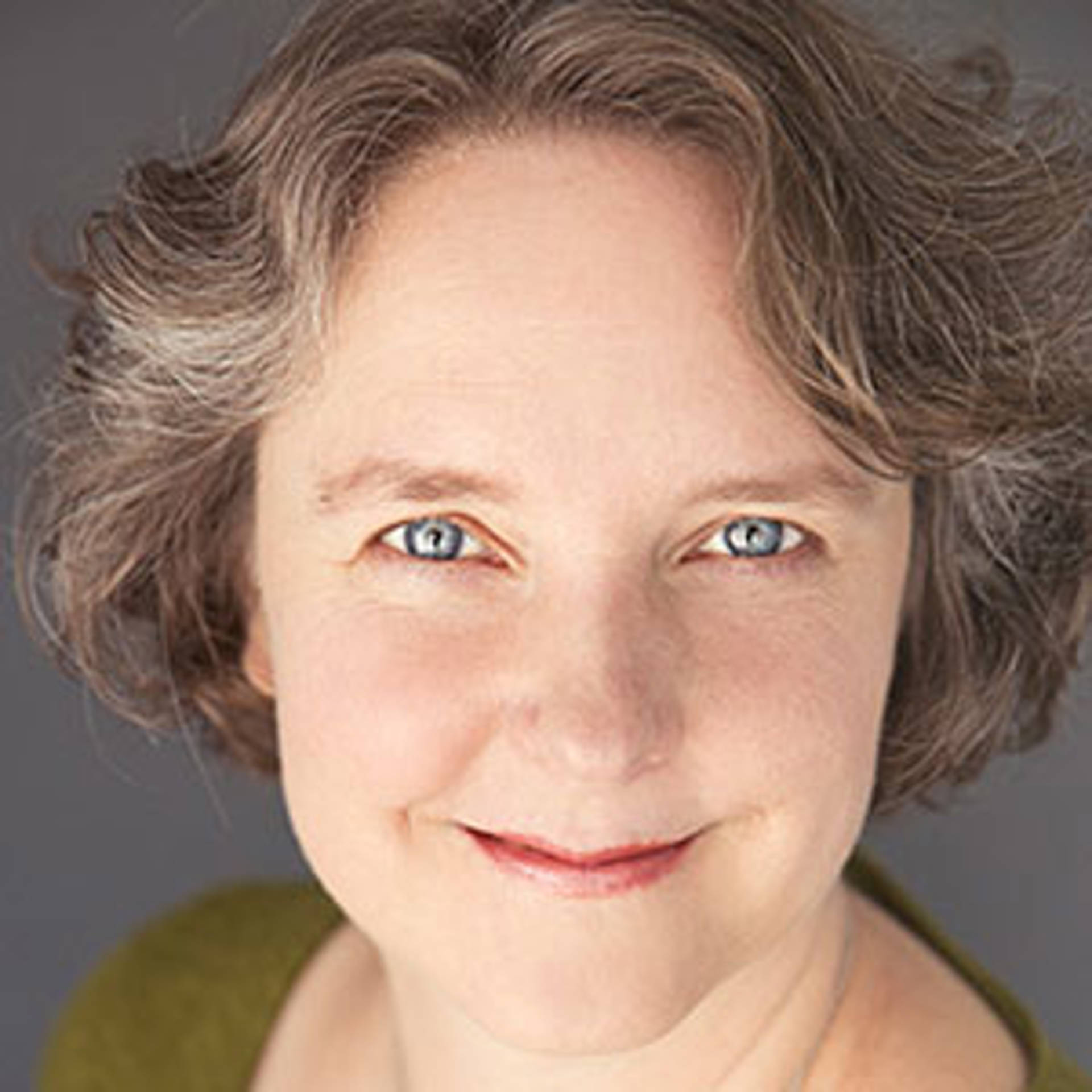Headshot of a middle aged caucasian woman with short brown and grey hair and blue eyes.