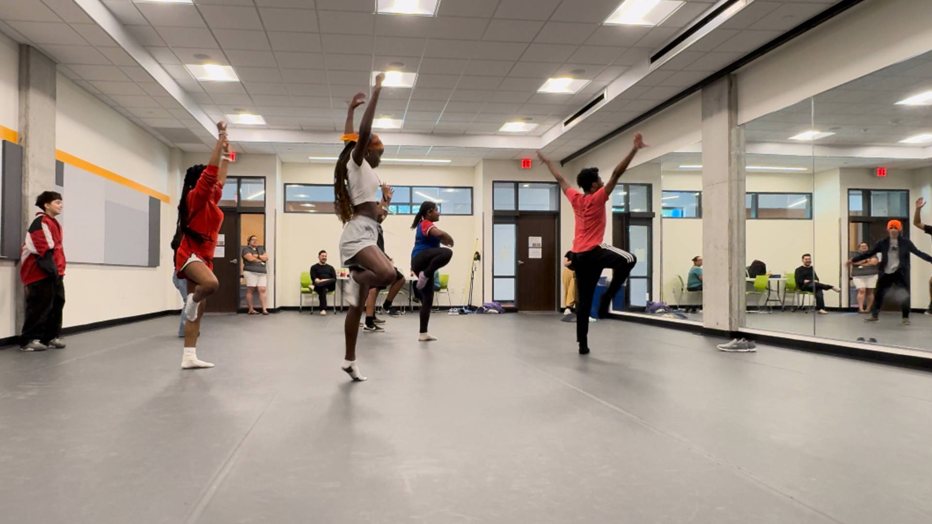 students dancing in a studio facing a large mirror. Their arms are up in the air.