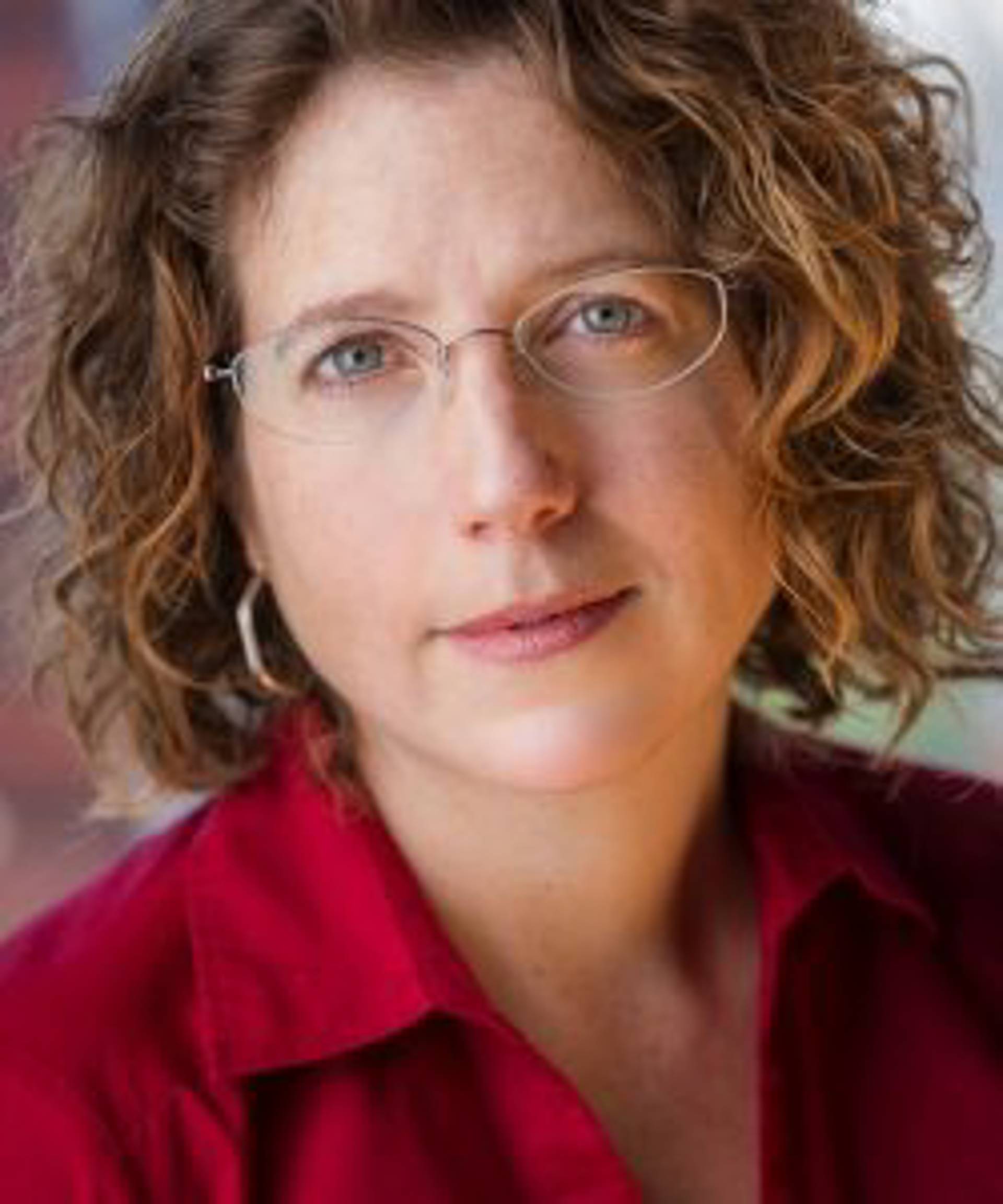 Headshot of a caucasian woman with wavy medium length hair and light blue eyes and glasses.