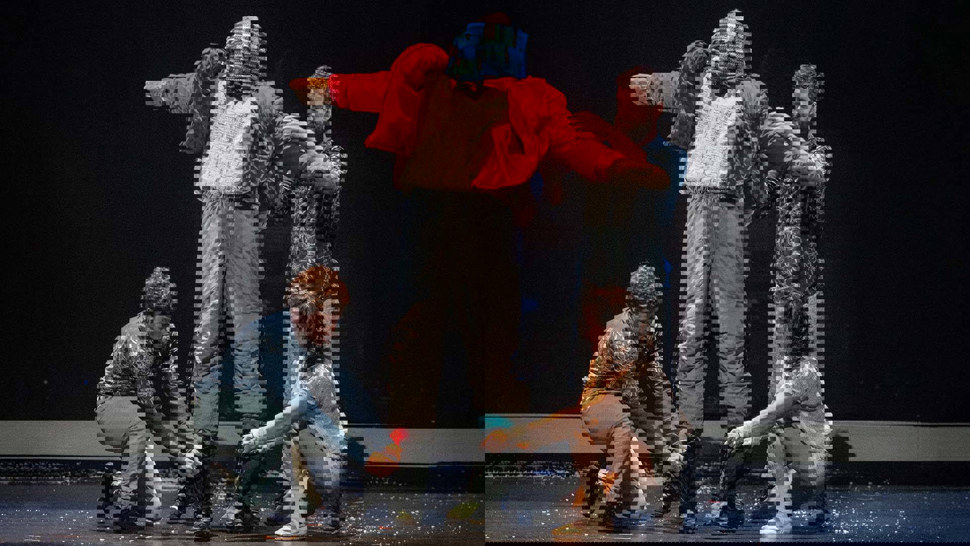 Three performers dressing up a scarecrow-like figure in winter clothing.