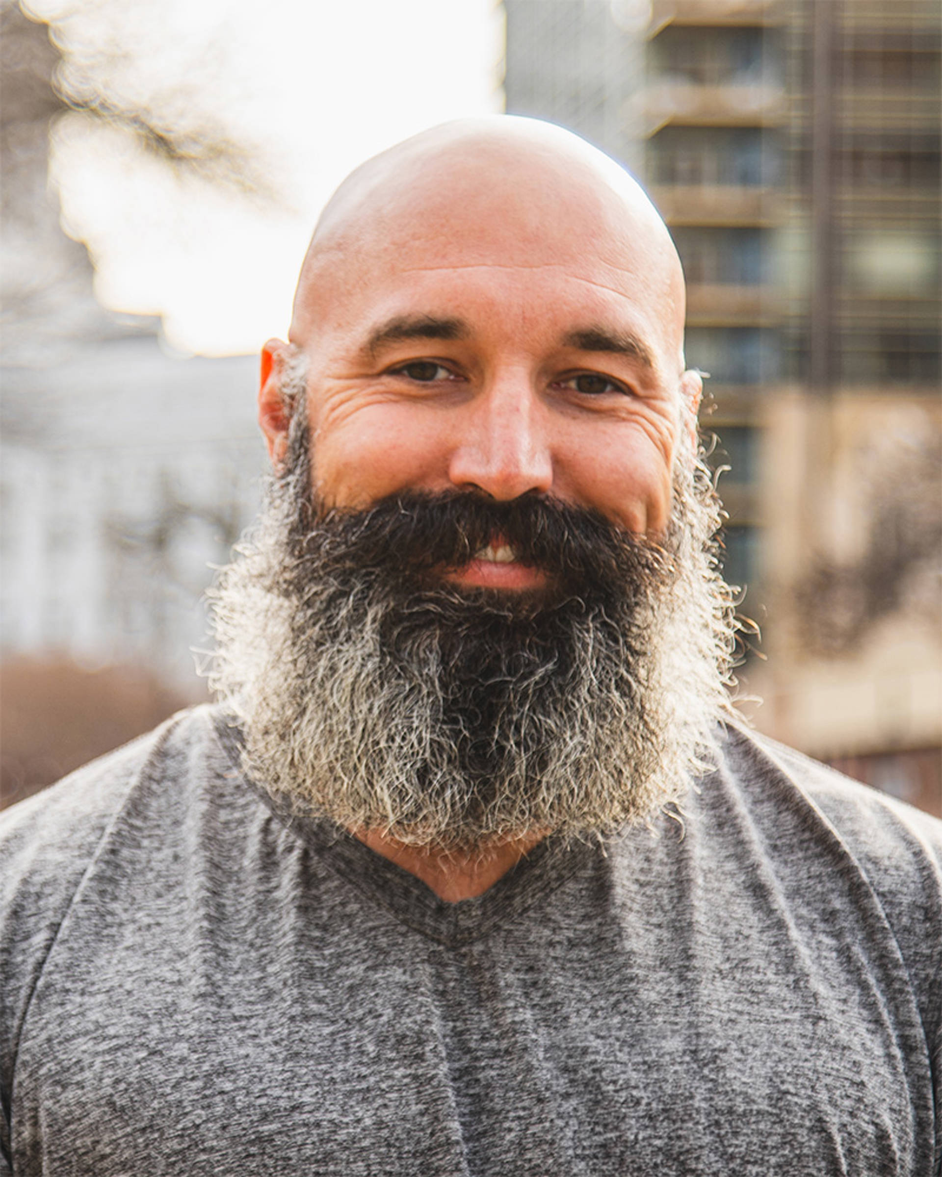 Headshot of a smiling white man with a bald head, large black and grey beard and dark eyes.