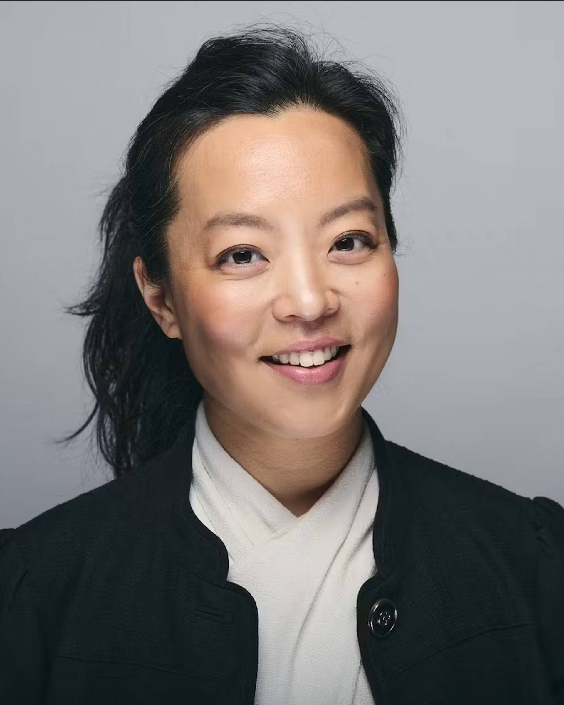 Headshot of a young woman with medium tone skin, dark long hair, and brown eyes in a white top with a dark jacket.