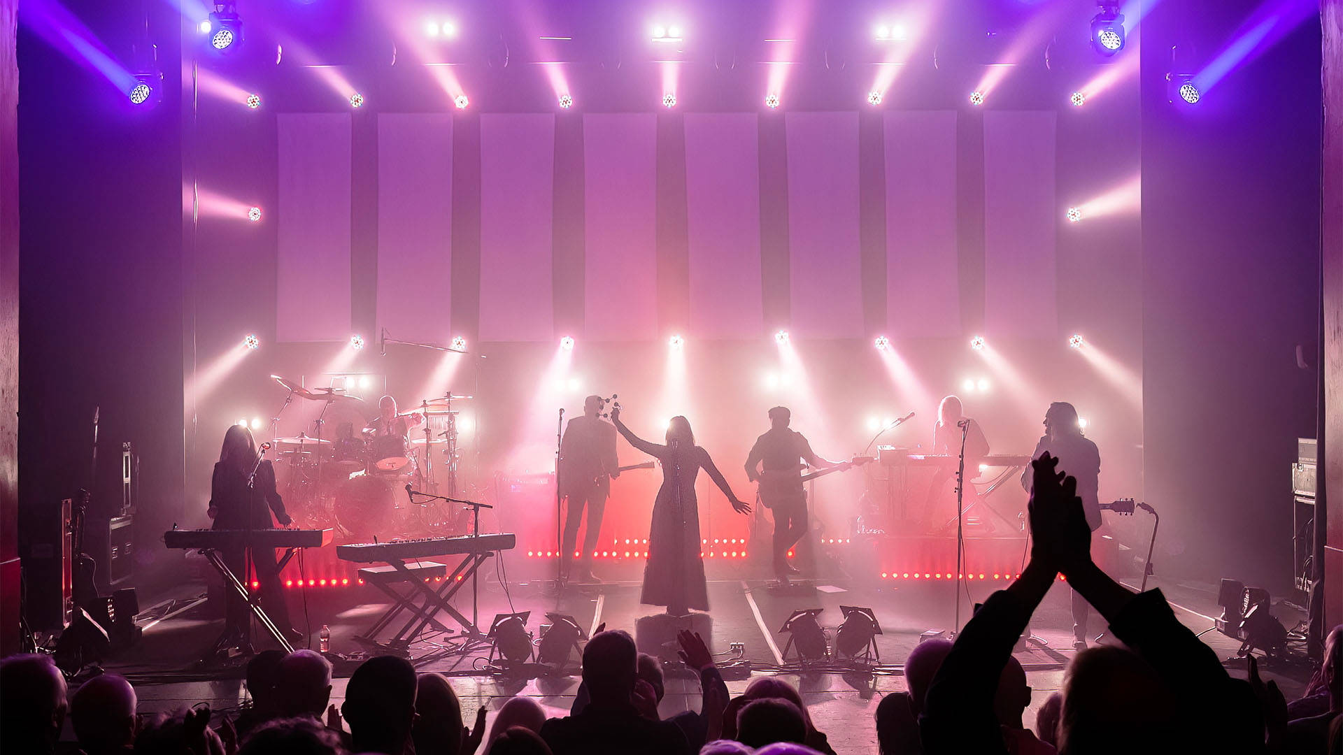 Rumours of Fleetwood Mac, a seven piece band, performing on stage to a standing audience.