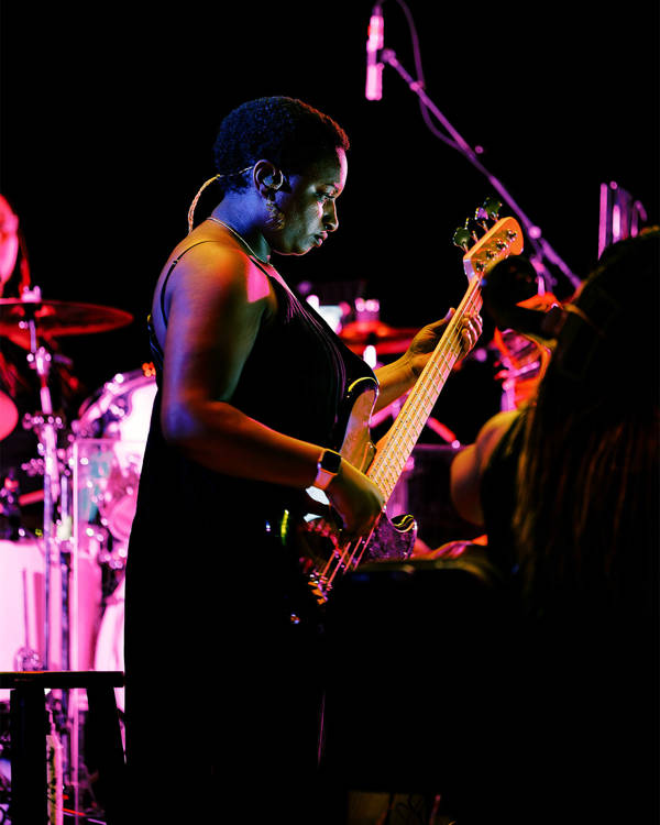 A woman with dark complexion and short dark hair in a dark top playing an electric bass.
