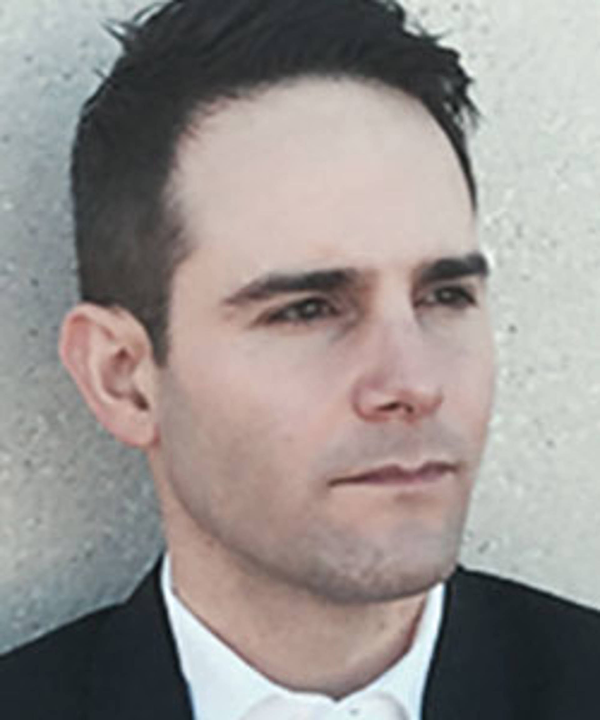 Headshot of a caucasian man with dark eyes and short brown. He is wearing a black suit jacket and white dress shirt.