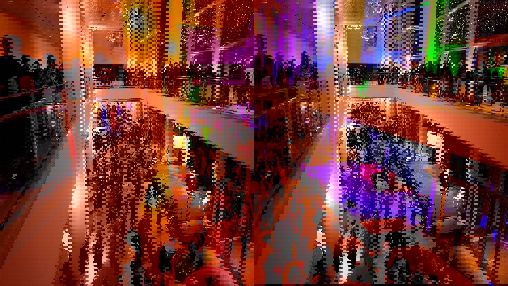 A wide shot of a large lobby space filled with people dancing and lit up with many different colors.