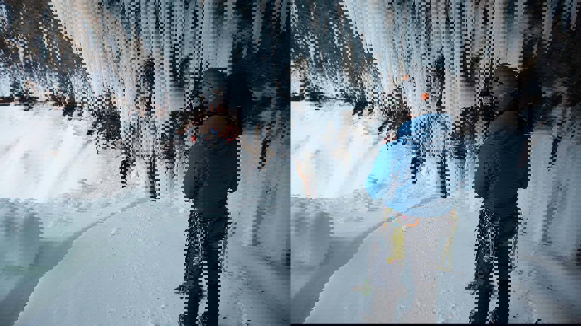 A cameraman wearing ice climbing gear with video camera over his shoulder shooting climbers in an icy cave.