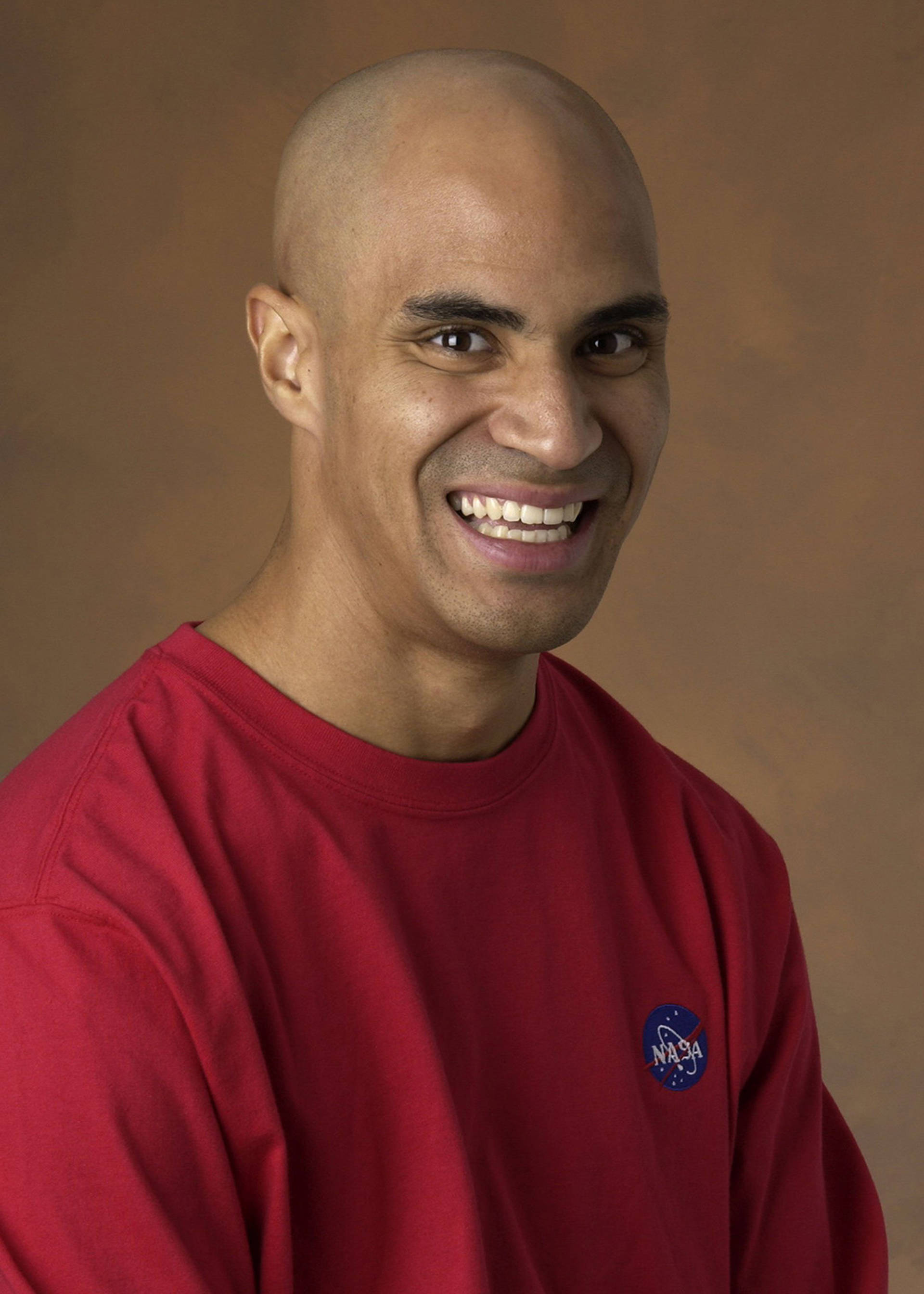 Portrait of Kobie Boykins. A medium-skinned Black man wearing a red crewneck sweater with NASA's logo. He is bald and smiling to the camera.
