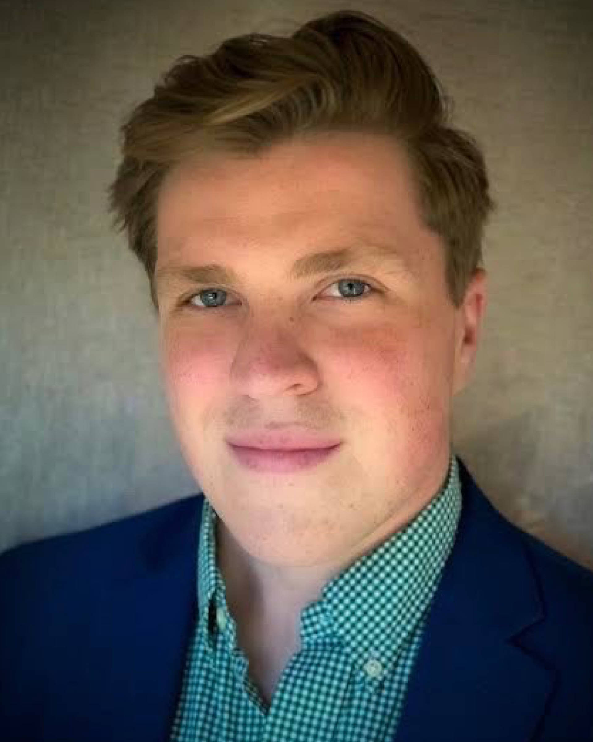 Headshot of a caucasian man with short brown hair, blue eyes, and blue jacket with green dress shirt.