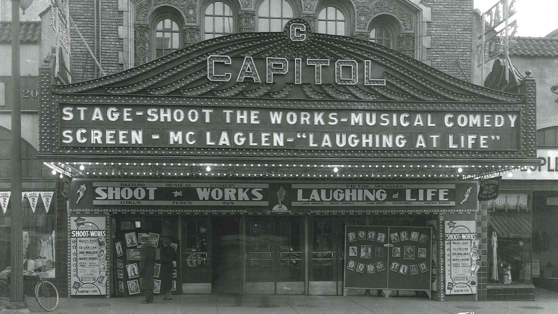 A black and white photo of the outside of Capitol Theater circa 1928. The marquee reads "Capitol. Stage-Shoot the Works-musical comedy. Screen-McLaglen-'Laughing at Life'"