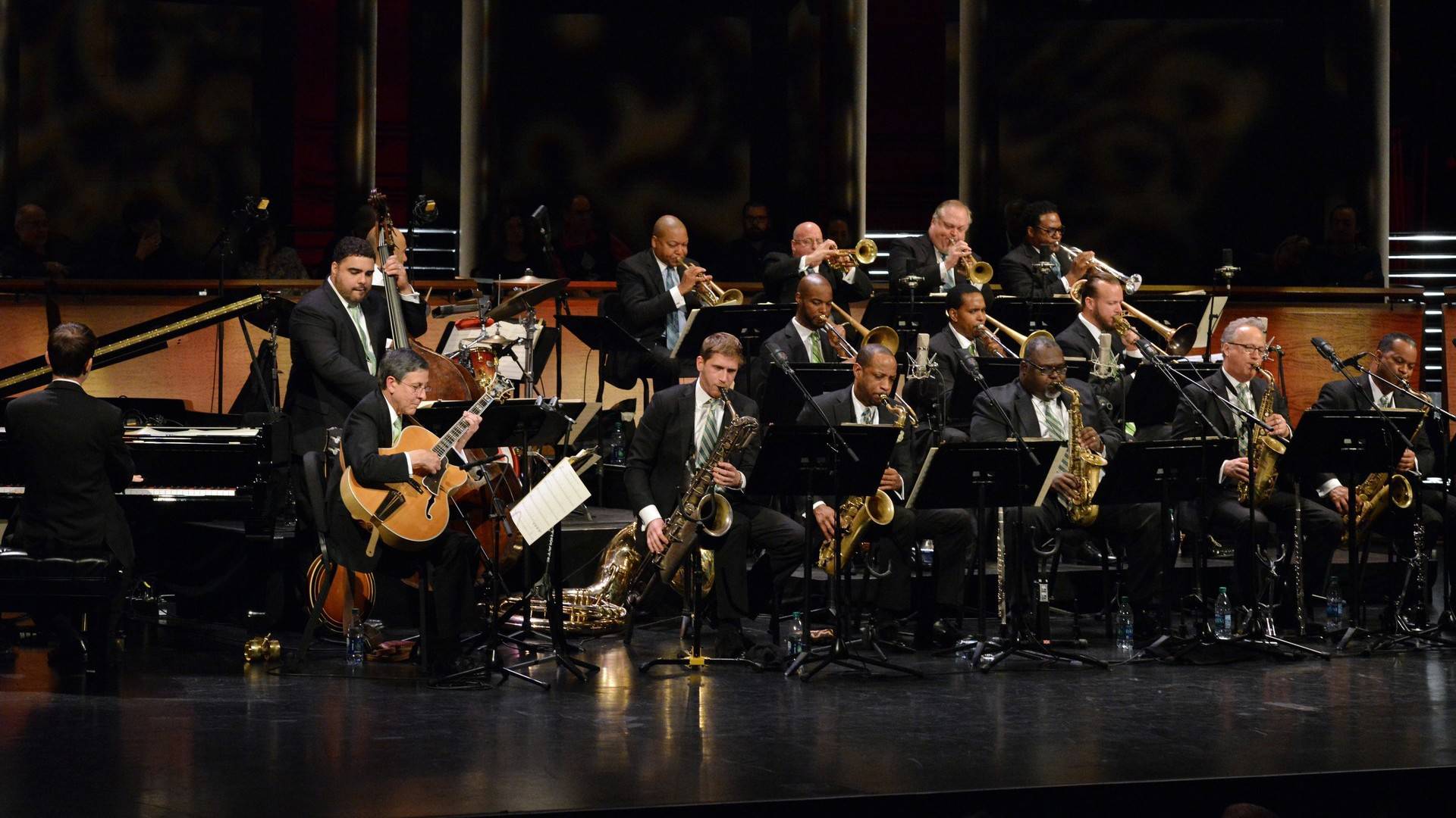 A jazz orchestra performing on a bandstand. They are all wearing suits.