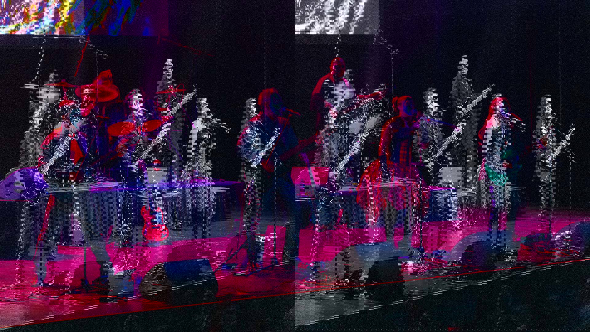 Members of Mariachi Rock Revolution, wearing black and white face paint, strum guitars and sing into microphones at the front of the stage.