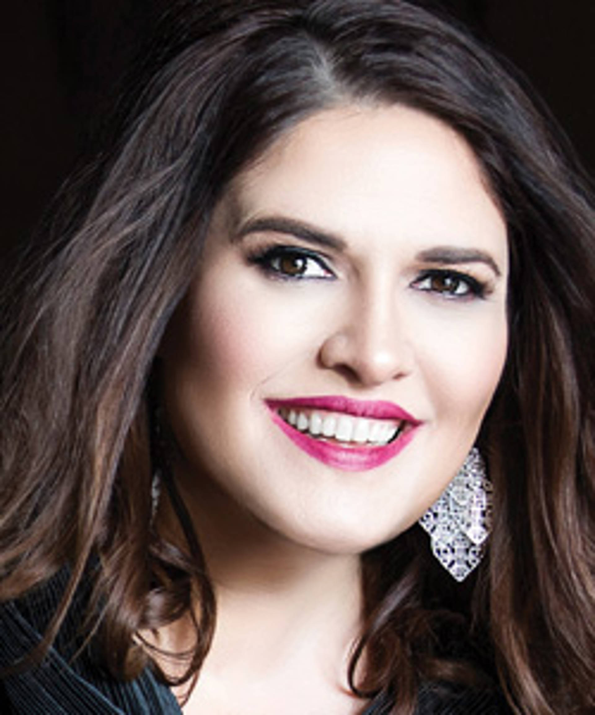 A light skinned woman with long brown hair lipstick and brown eyes.