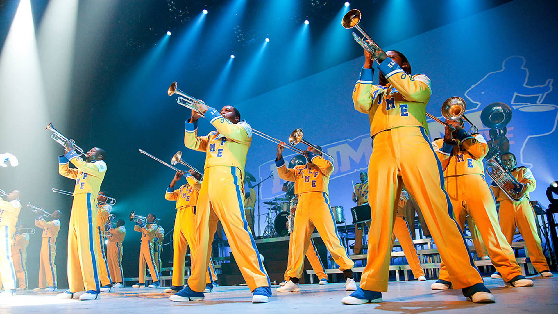 An African-American marching band performing on stage wearing yellow and blue uniforms.