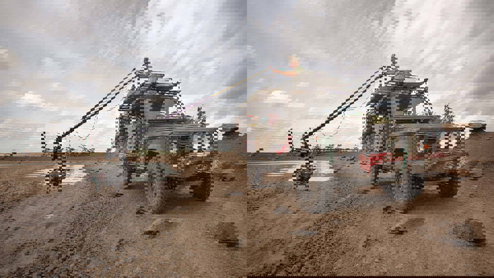 A videographer with a camera on a long boom mounted to the top of an offroad vehicle.