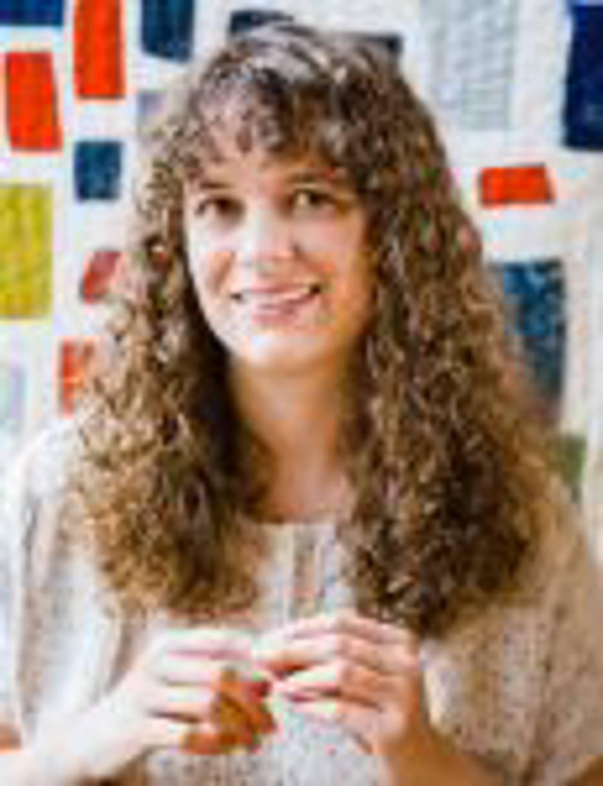 Haedshot of a middleaged caucasian woman with curly brown hair and a tan top on.
