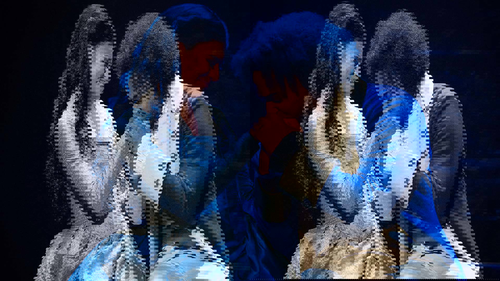 A man with medium-length curly hair and a dark complexion kisses the hand of a woman with a medium complexion and long, dark hair.