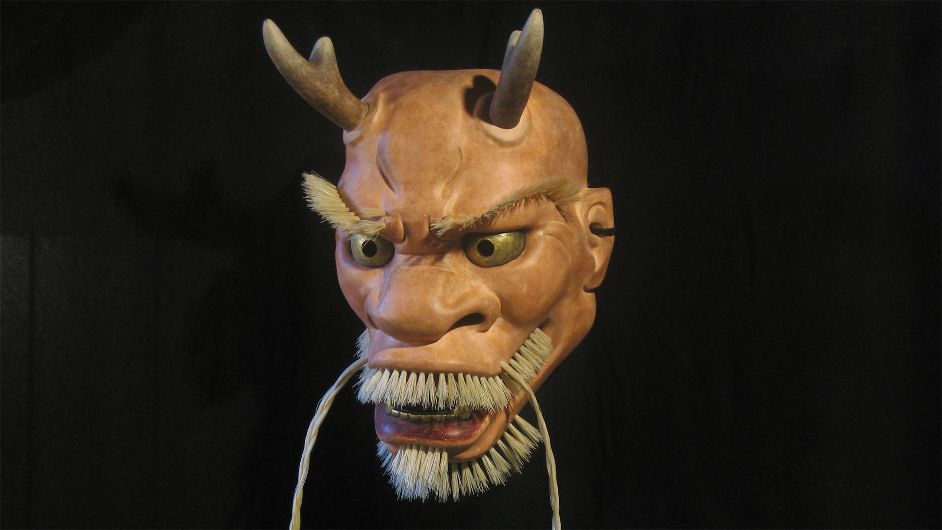 A ceramic mask of a dragon head with horns and a beard.