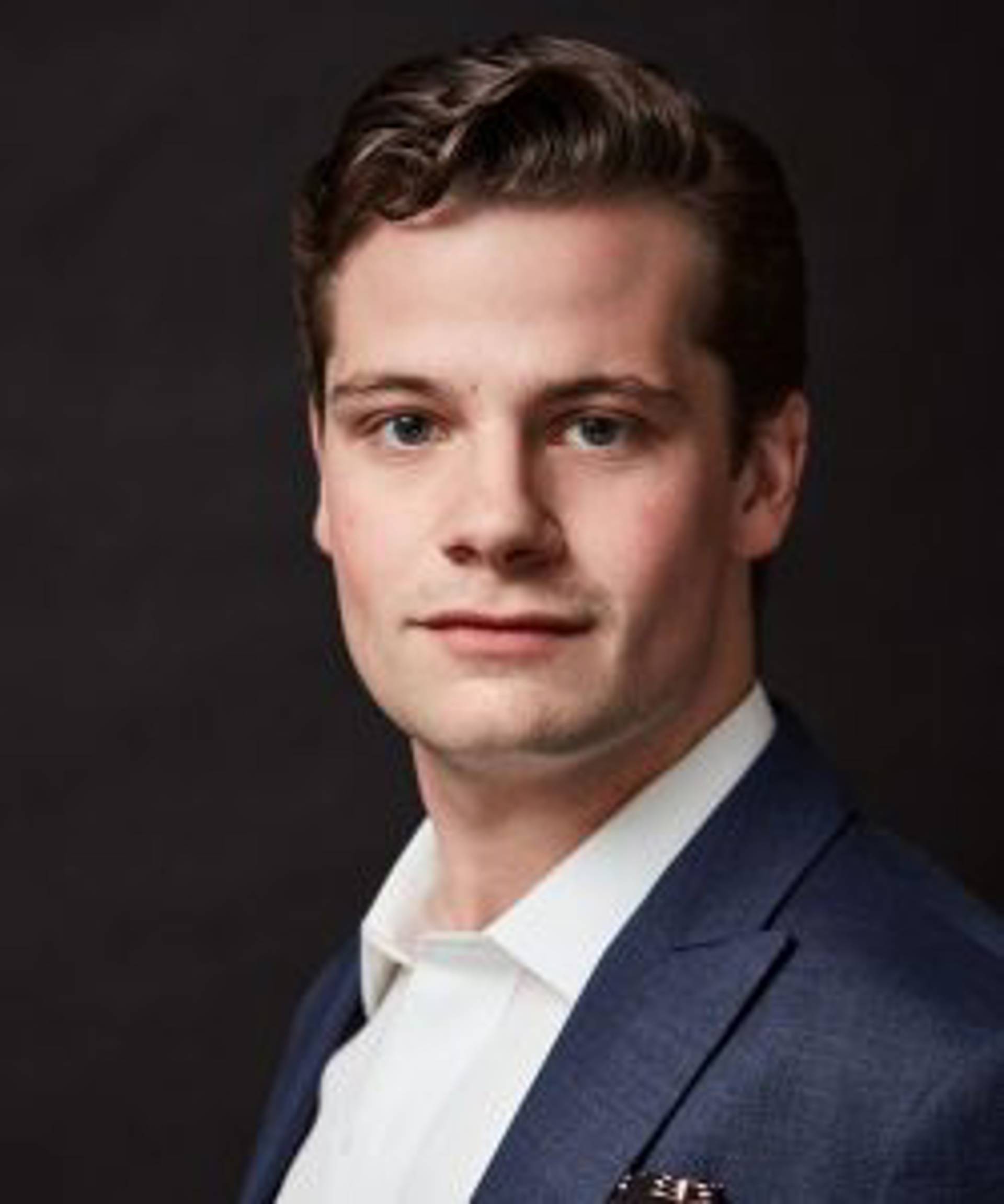 Headshot of a caucasian many with short wavy brown hair and dark eyes in a blue suit.
