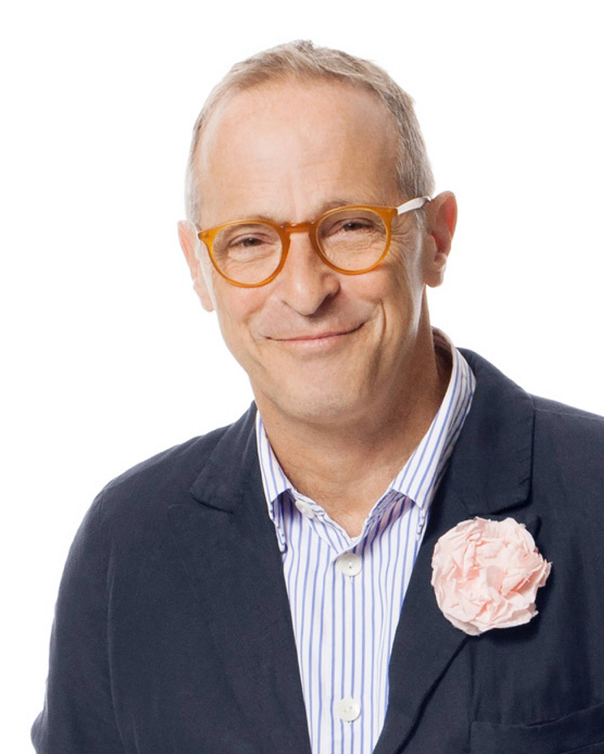 A photo of David Sedaris, an older white man in a blue suit with brown glasses smiling towards the viewer.