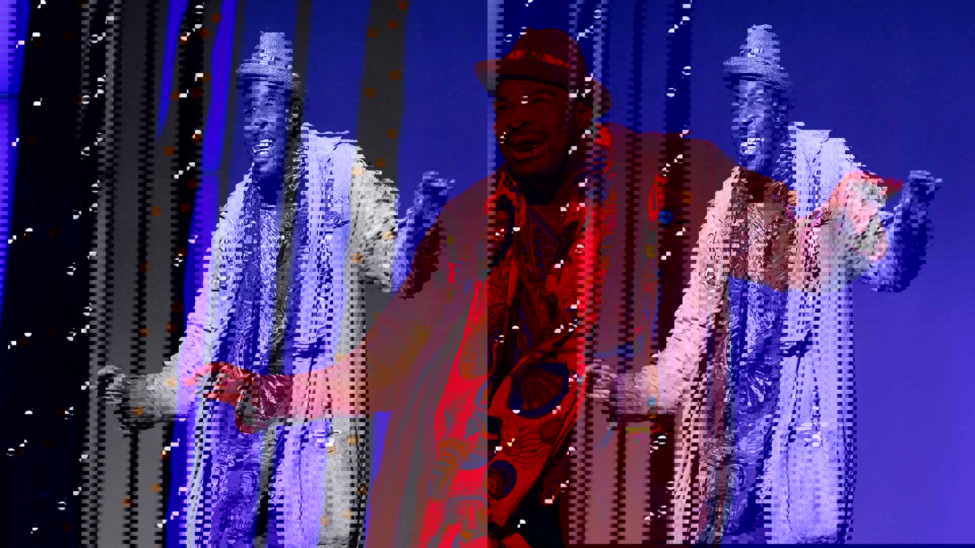An African American Man in colorful baggy clothing and a hat dances on stage