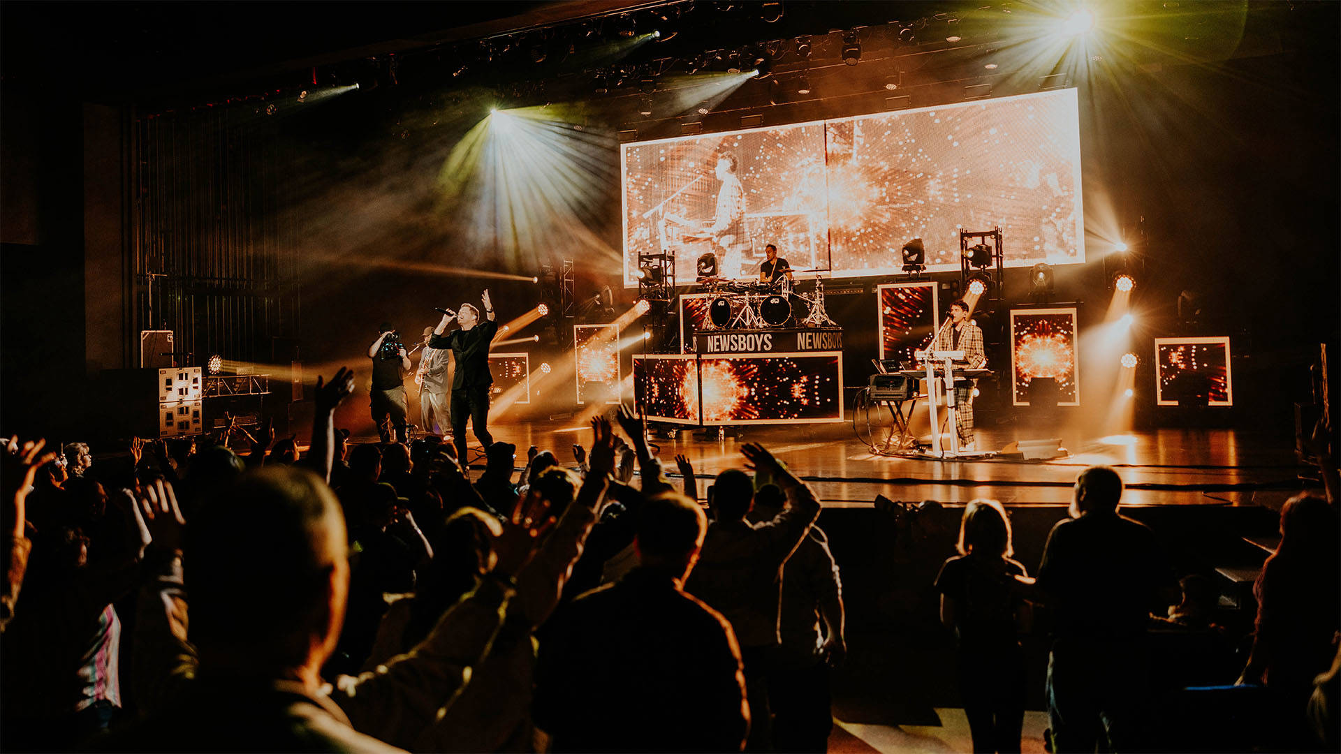wide shot of a band playing on a stage with an audience watching in the foreground.