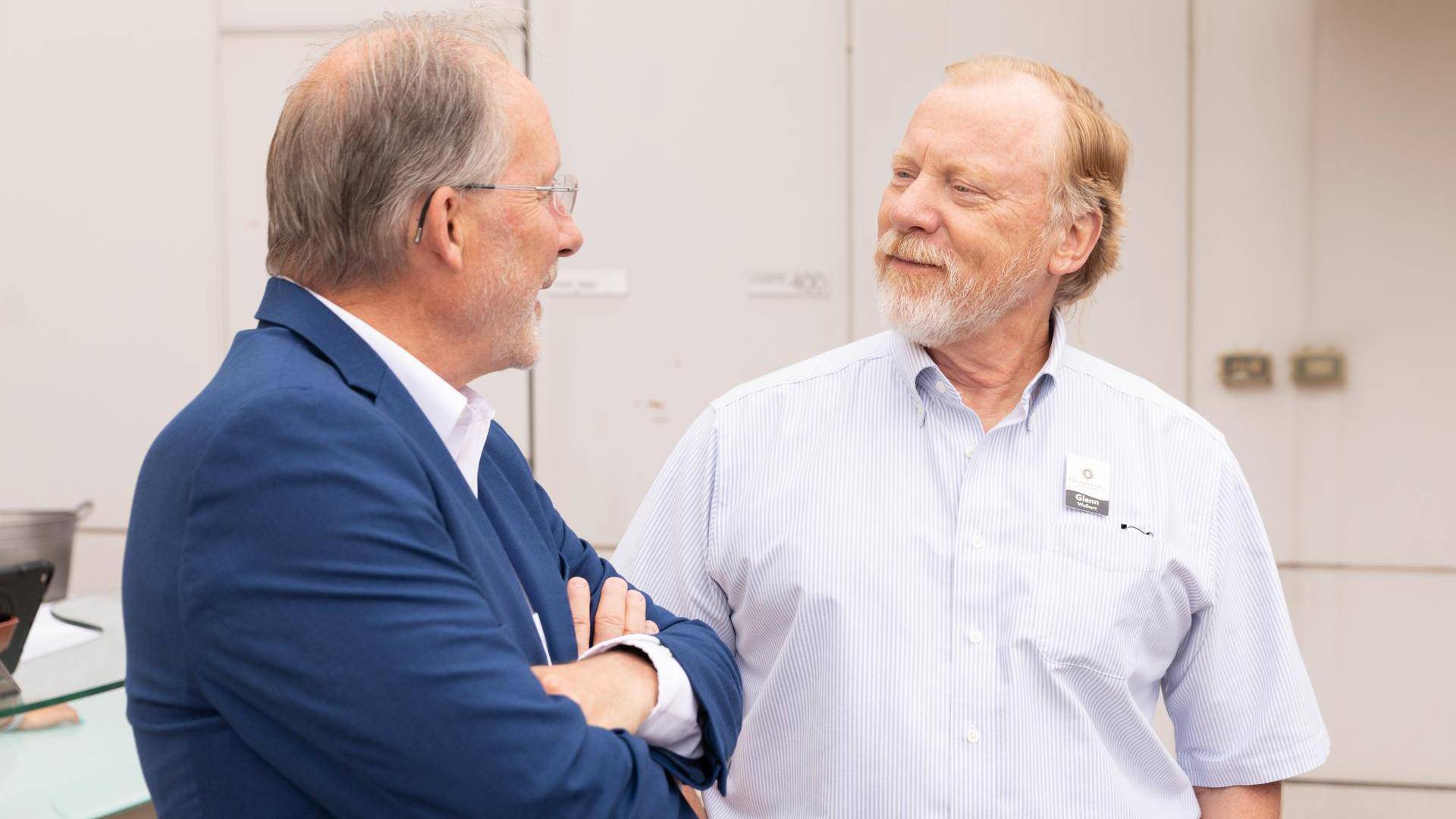 Two middle aged men with light complexion stand and talk.