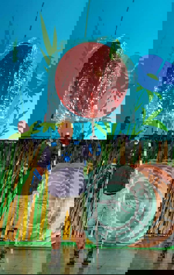 Martin Kratt, a man with light complexion wearing safari clothes and a black vest and gloves, holds a giant red lollipop during a LIVE 2.0 performance.