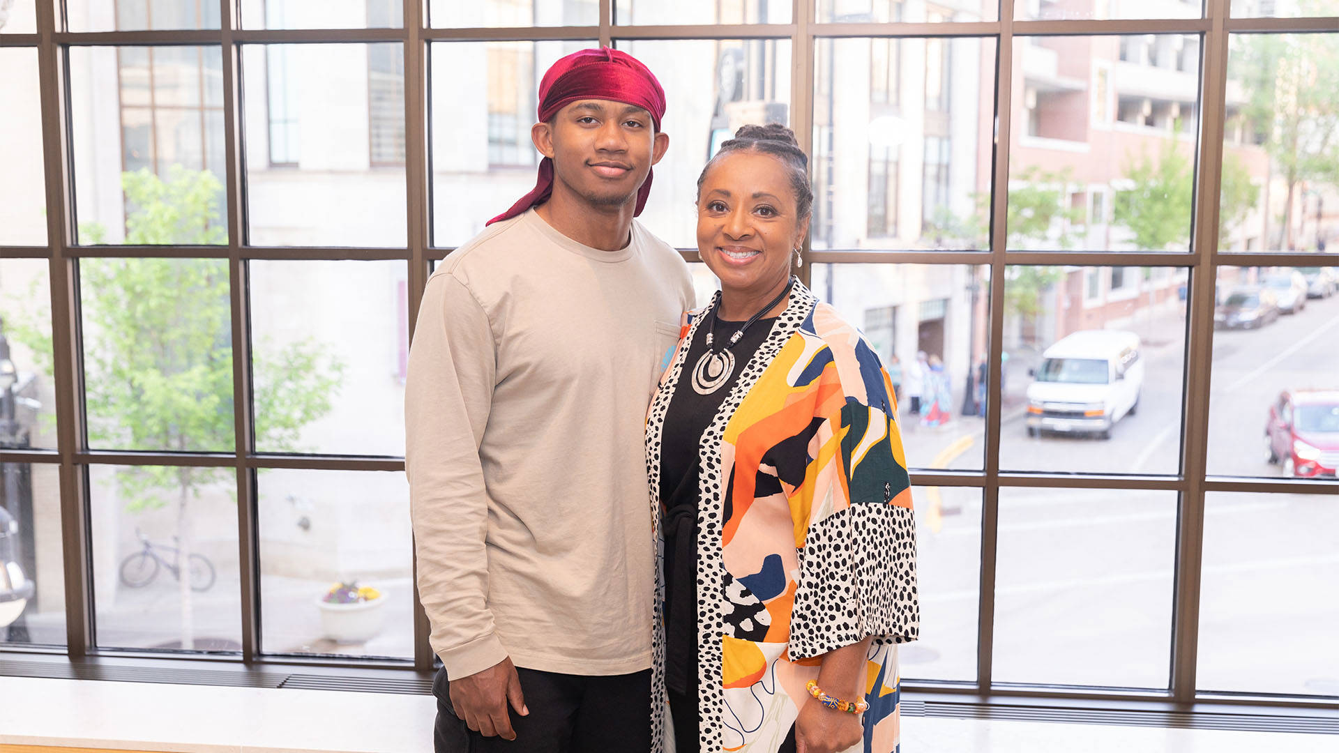 An African American woman in colorful clothing poses for a photo with a young African American man in a tan shirt.