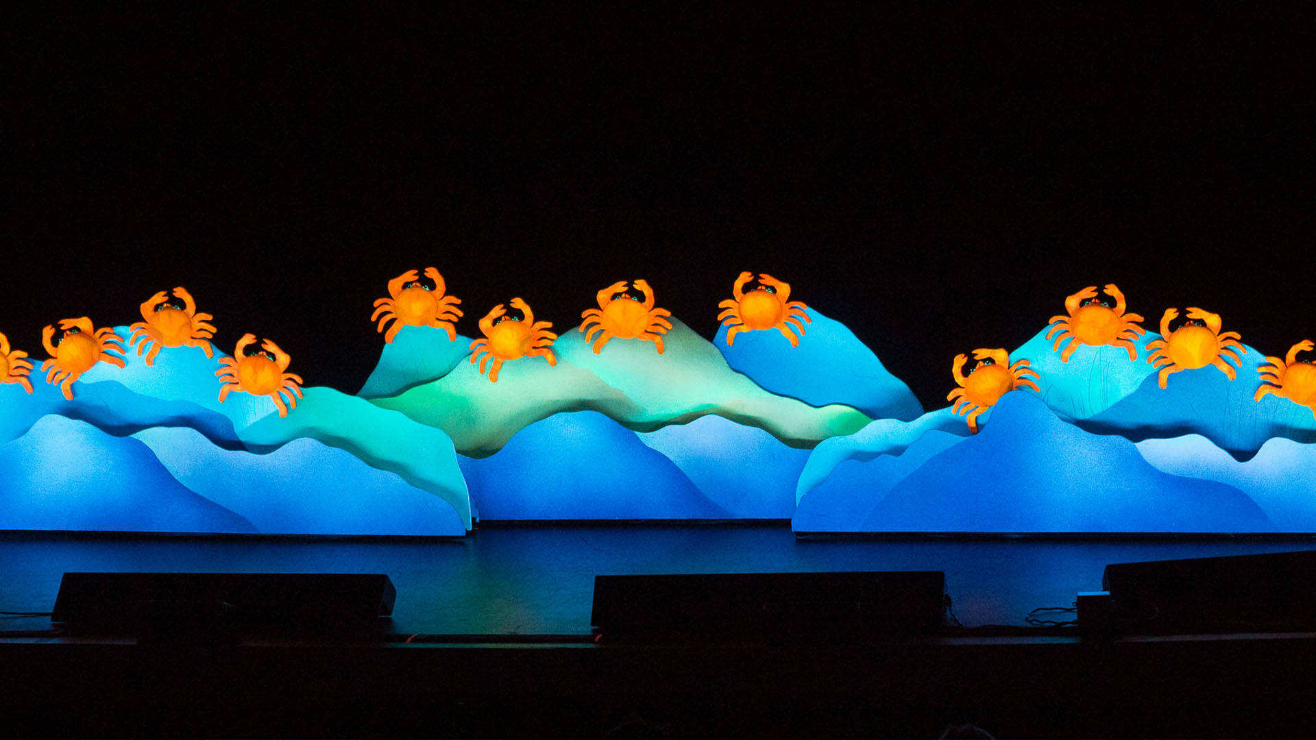 Eleven orange puppet crabs sitting on blue rocks.