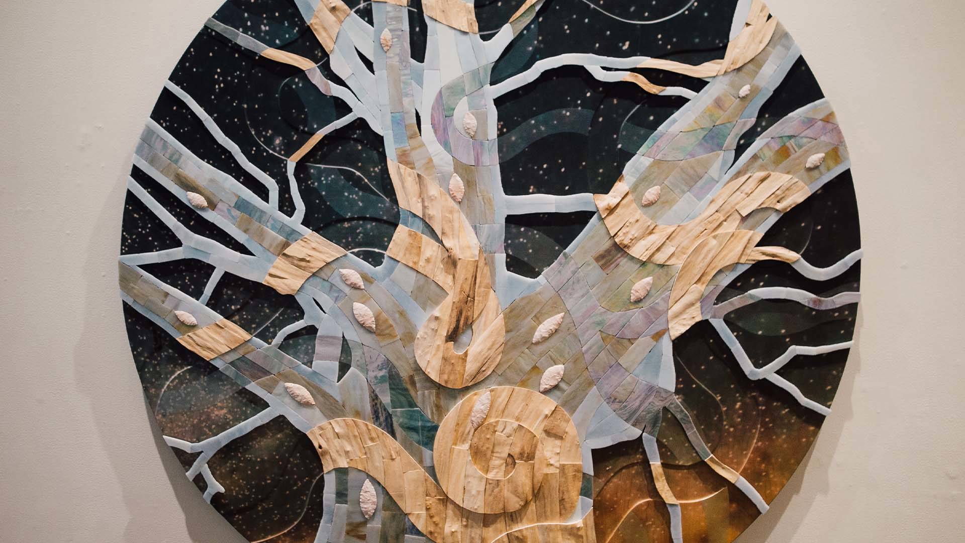 A wood, circular piece of art. It shows a tree with many branches.