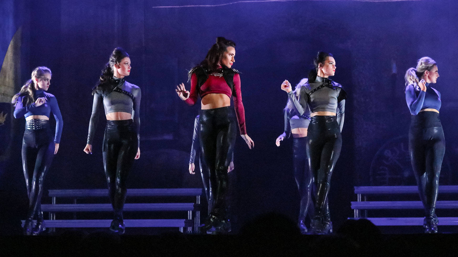 A group of Irish dancers in red black and silver outfits performing on stage. They are all in a similar pose.