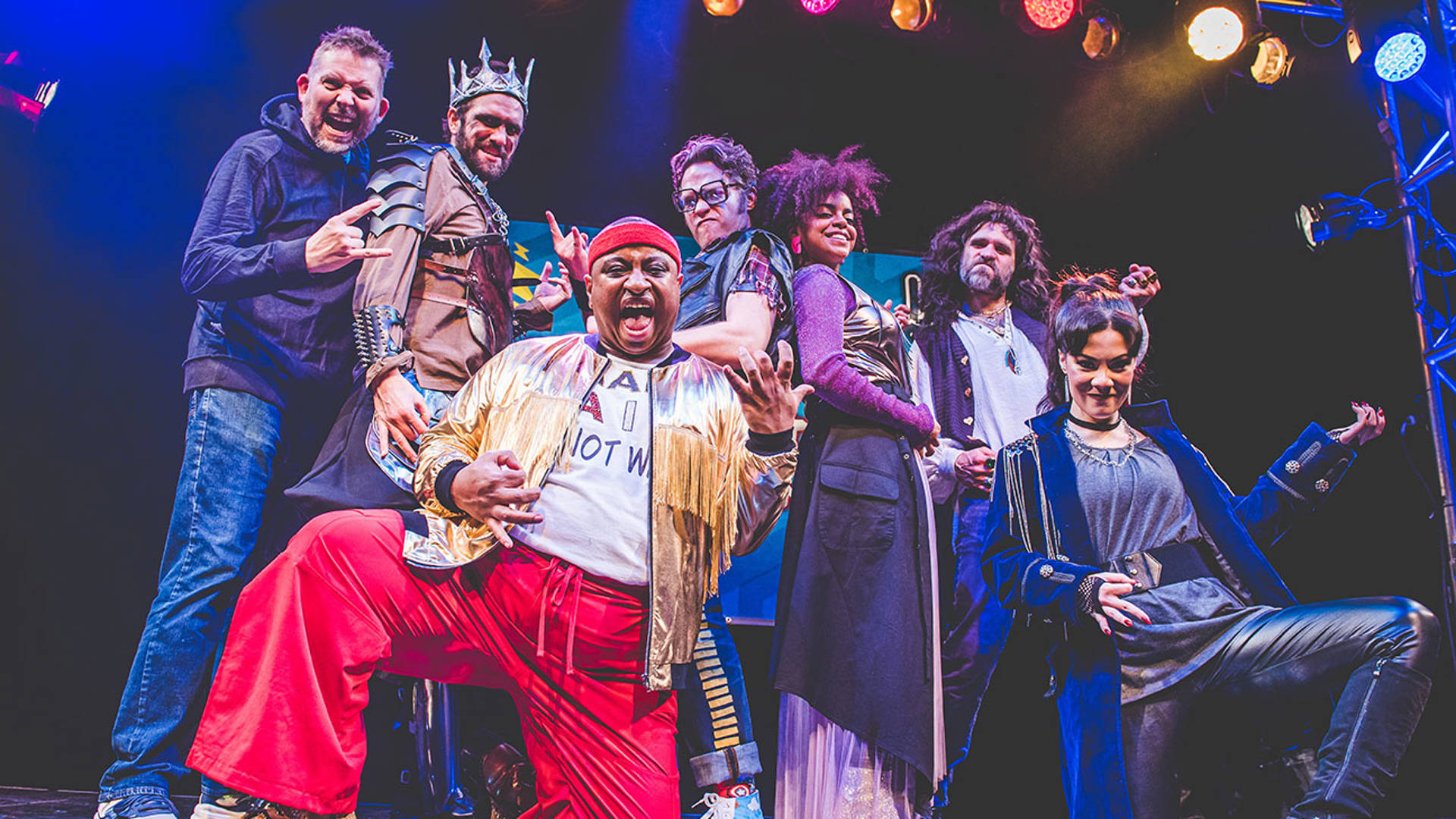 A cast with zany rock and roll outfits miming air guitar.