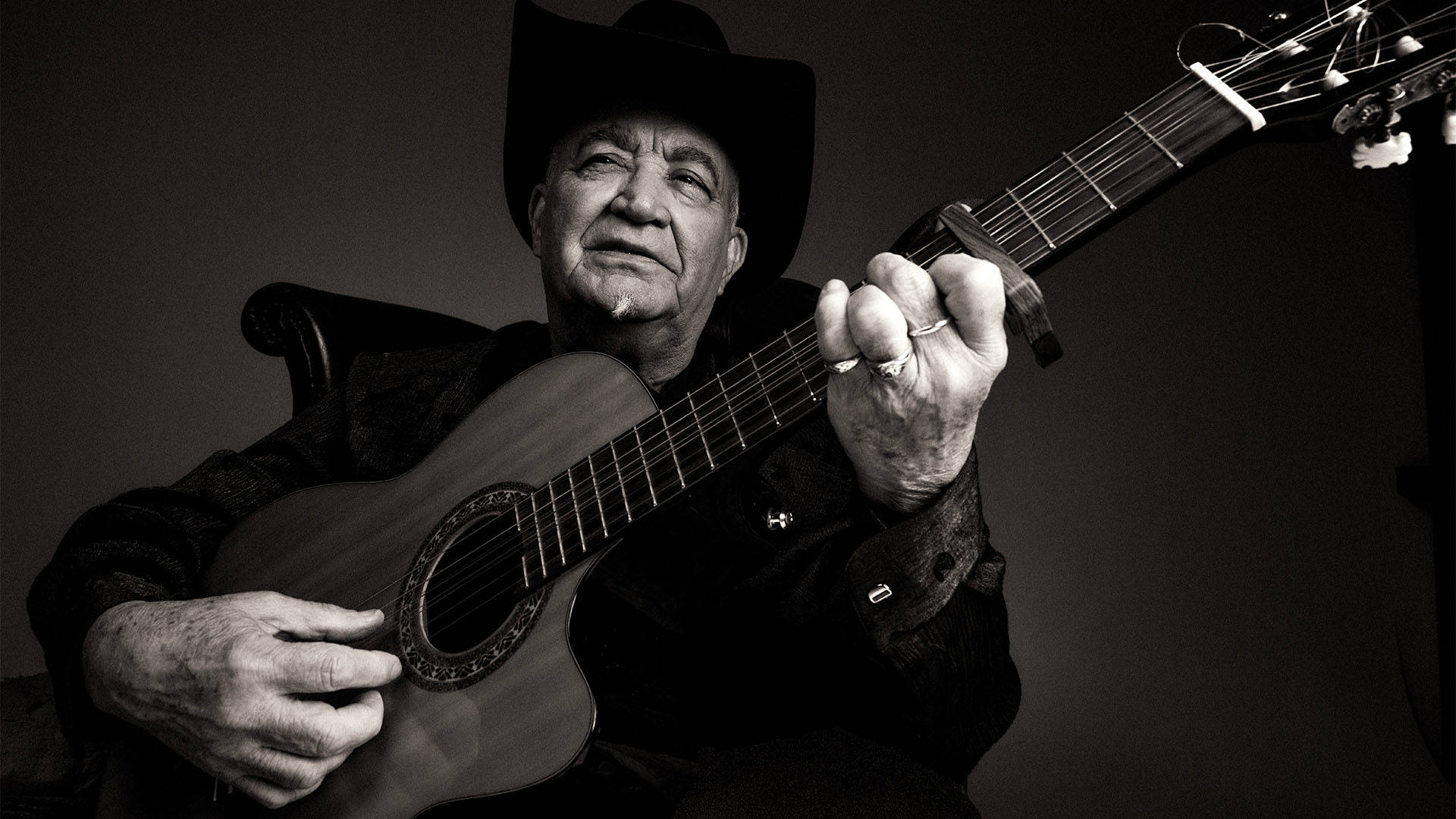 Eliades Ochoa in black and white playing the guitar.