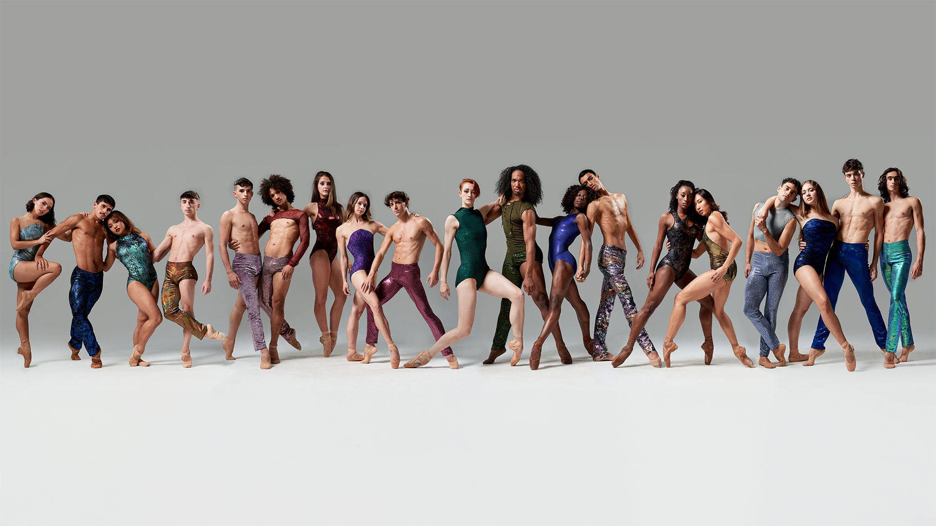 Contemporary dancers standing together in a long line against a grey background.
