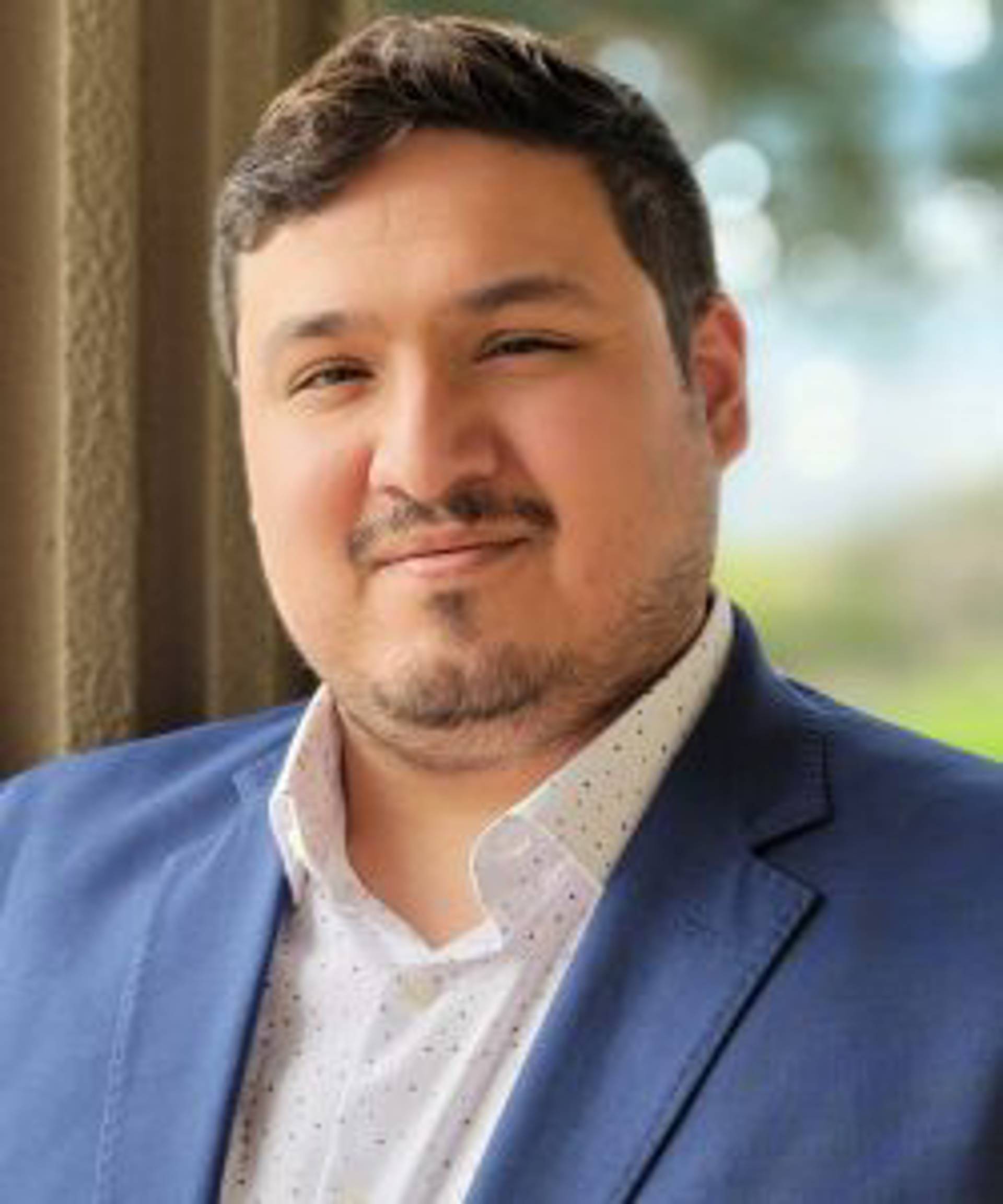 Headshot of a man with brown hair and light facial hair in a blue suit.