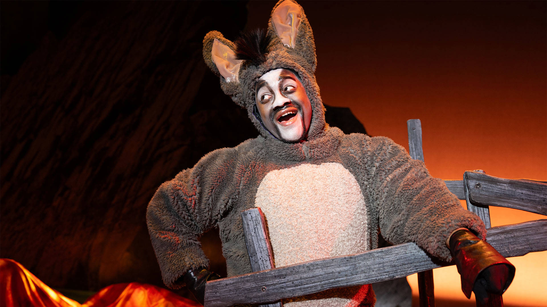 A black man in a grey Donkey onesie costume with large ears and face paint.